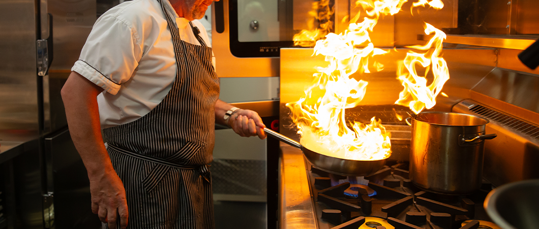 A photo of a chef flaming a fry pan.
