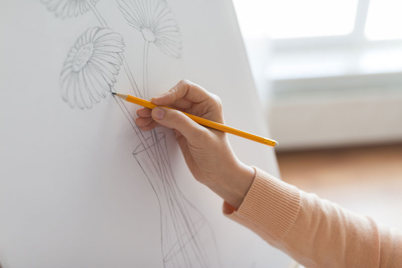 Image of a hand doing a drawing of a flower on an easel 